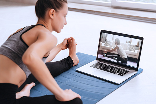 Fit woman in sportswear doing yoga on exercise mat at home using laptop watching tutorial. Female coach has a virtual yoga class on computer. Healthy and active lifestyle concept. Online home training